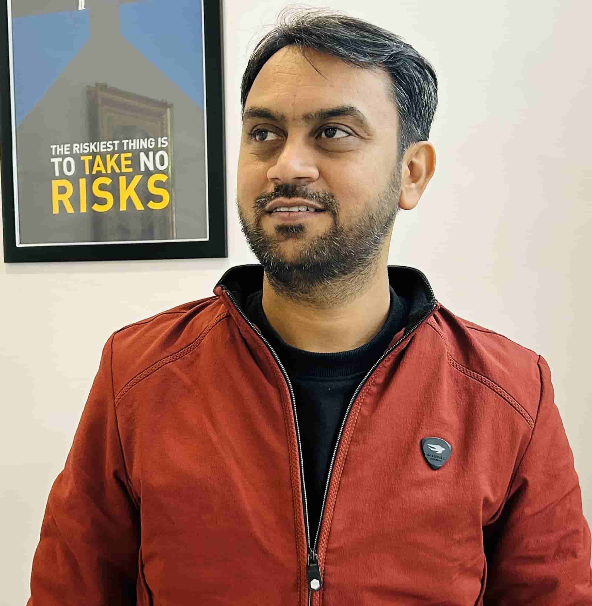 Shyam Verma portrait next to a "The riskiest thing is to take no risks" poster